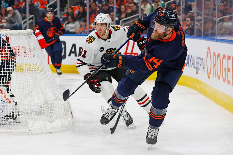 Jan 25, 2024; Edmonton, Alberta, CAN; Edmonton Oilers defensemen Mattias Ekholm (14) clears the puck in front of Chicago Blackhawks forward Taylor Raddysh (11) during the second period at Rogers Place. Mandatory Credit: Perry Nelson-USA TODAY Sports