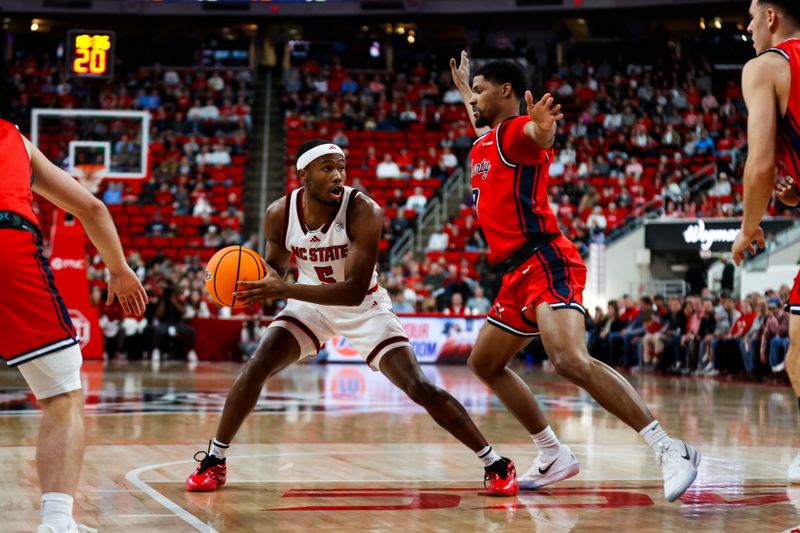 Dec 6, 2025; Raleigh, North Carolina, USA; NC State Wolfpack guard Tre Holloman (5) with the ball goaded by Liberty Flames guard JJ Harper (9) during the first half of the game at Lenovo Center. Mandatory Credit: Jaylynn Nash-Imagn Images