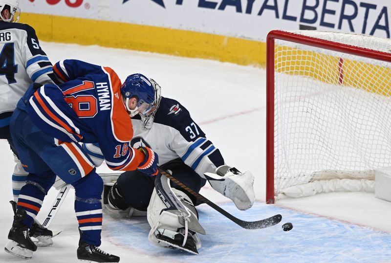 Mar 20, 2025; Edmonton, Alberta, CAN; Edmonton Oilers left winger Zach Hyman (18) goes for a shot on Winnipeg Jets goalie Connor Hellebuyck (37) during the third period at Rogers Place. Mandatory Credit: Walter Tychnowicz-Imagn Images