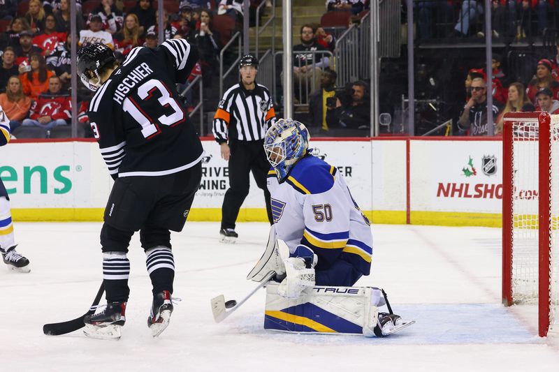 Nov 27, 2024; Newark, New Jersey, USA; St. Louis Blues goaltender Jordan Binnington (50) makes a save through a screen by New Jersey Devils center Nico Hischier (13) during the second period at Prudential Center. Mandatory Credit: Ed Mulholland-Imagn Images