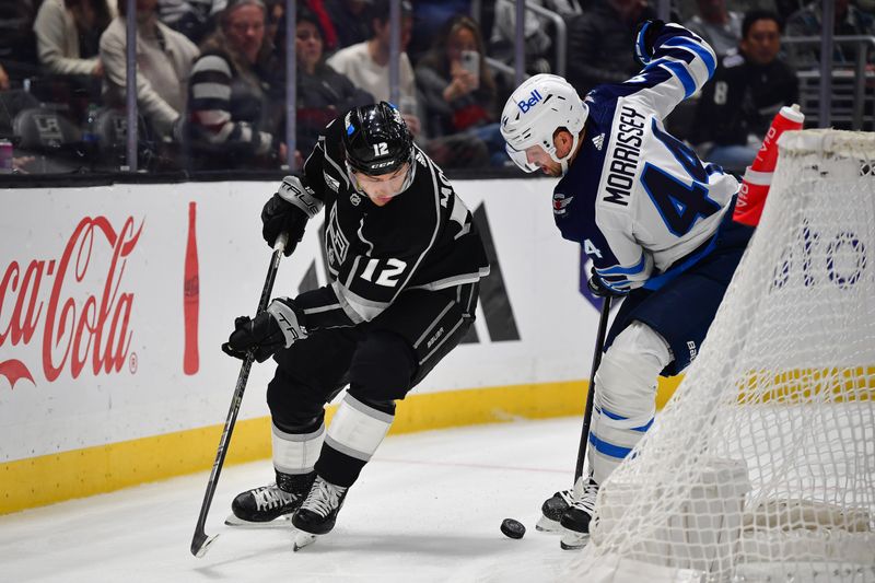 Dec 13, 2023; Los Angeles, California, USA; Los Angeles Kings left wing Trevor Moore (12) plays for the puck against Winnipeg Jets defenseman Josh Morrissey (44) during the second period at Crypto.com Arena. Mandatory Credit: Gary A. Vasquez-USA TODAY Sports