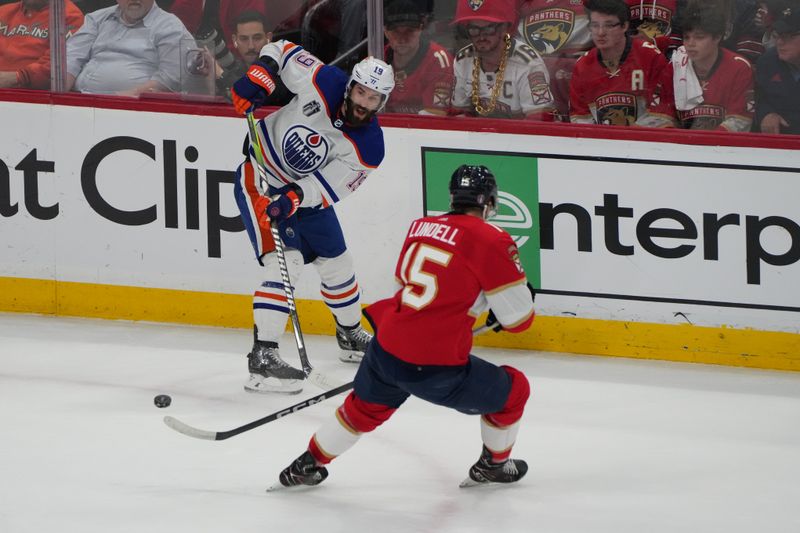 Jun 24, 2024; Sunrise, Florida, USA; Edmonton Oilers forward Adam Henrique (19) and Florida Panthers forward Anton Lundell (15) reach for the puck during the first period in game seven of the 2024 Stanley Cup Final at Amerant Bank Arena. Mandatory Credit: Jim Rassol-USA TODAY Sports