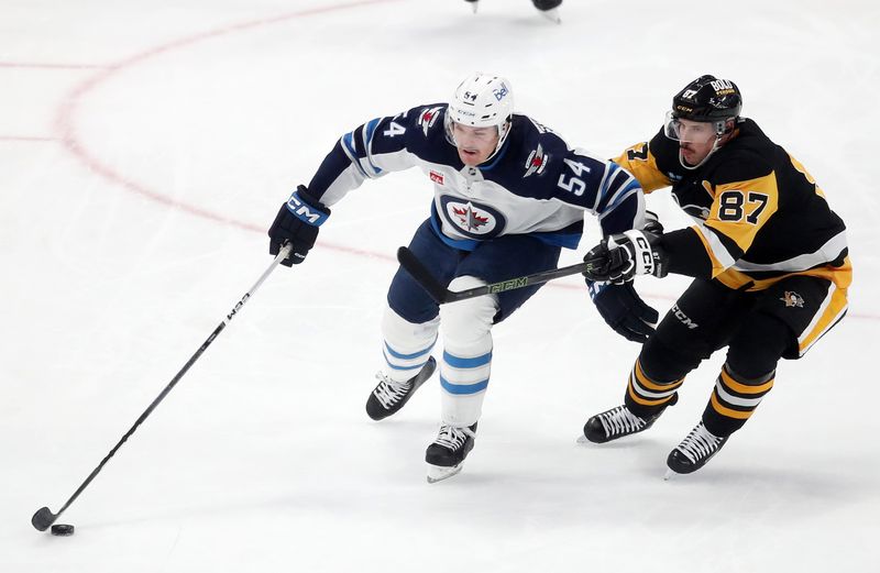 Nov 22, 2024; Pittsburgh, Pennsylvania, USA;  Winnipeg Jets defenseman Dylan Samberg (54) chases the puck against pressure from Pittsburgh Penguins center Sidney Crosby (87) during the second period at PPG Paints Arena. Mandatory Credit: Charles LeClaire-Imagn Images