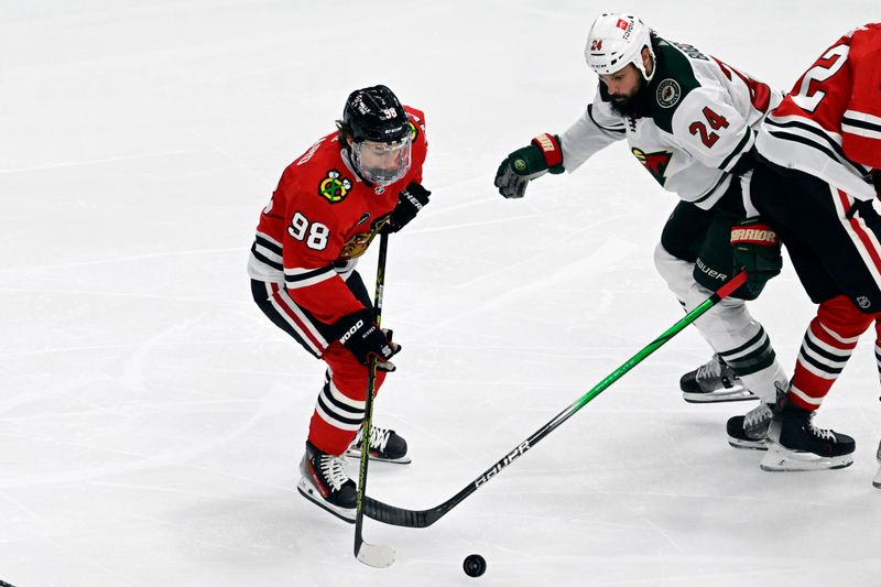 Apr 7, 2024; Chicago, Illinois, USA;  Chicago Blackhawks center Connor Bedard (98) and Minnesota Wild defenseman Zach Bogosian (24) chase the puck during the second period at United Center. Mandatory Credit: Matt Marton-USA TODAY Sports