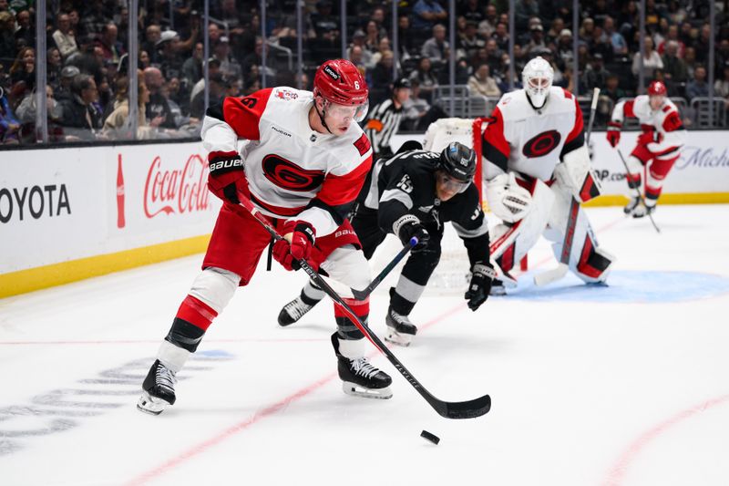 Oct 18, 2025; Los Angeles, California, USA; Carolina Hurricanes defenseman Mike Reilly (6) controls the puck under pressure from Los Angeles Kings right wing Quinton Byfield (55) during the second period at Crypto.com Arena. Mandatory Credit: William Liang-Imagn Images