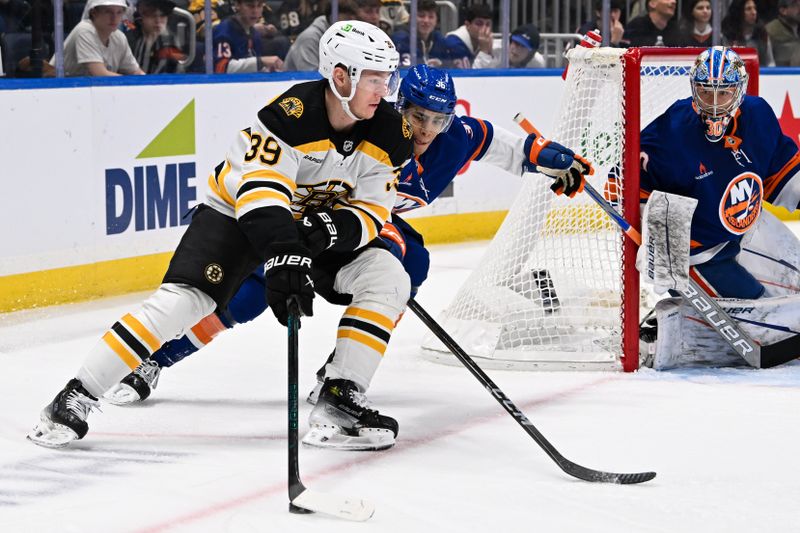 Nov 27, 2024; Elmont, New York, USA;  Boston Bruins center Morgan Geekie (39) skates the puck from behind the net chased by New York Islanders defenseman Isaiah George (36) during the first period at UBS Arena. Mandatory Credit: Dennis Schneidler-Imagn Images