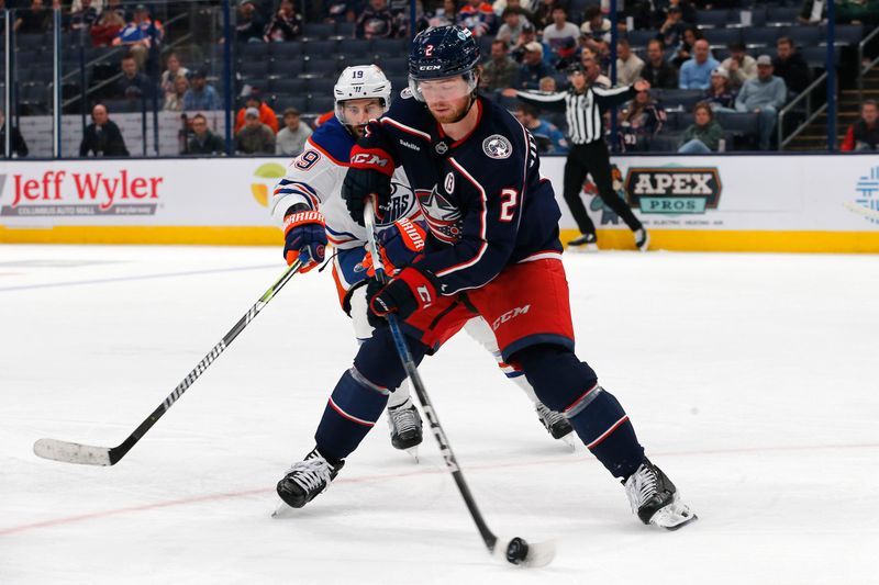 Oct 28, 2024; Columbus, Ohio, USA; Columbus Blue Jackets defenseman Jake Christiansen (2) clears a loose puck as Edmonton Oilers center Adam Henrique (19) trails the play during the third period at Nationwide Arena. Mandatory Credit: Russell LaBounty-Imagn Images