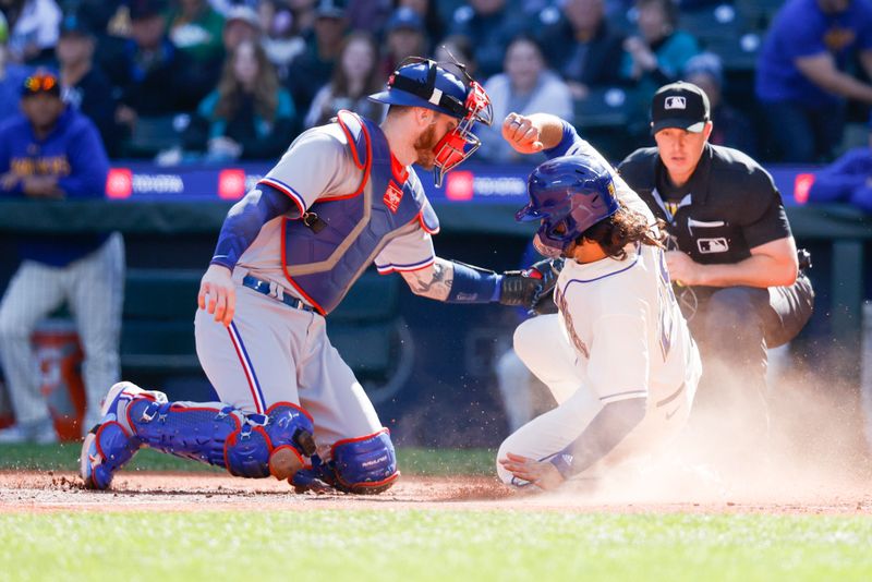 Oct 1, 2023; Seattle, Washington, USA; Seattle Mariners third baseman Eugenio Suarez (28, right) slides home to score a run against Texas Rangers catcher Jonah Heim (28) during the fourth inning at T-Mobile Park. Mandatory Credit: Joe Nicholson-USA TODAY Sports