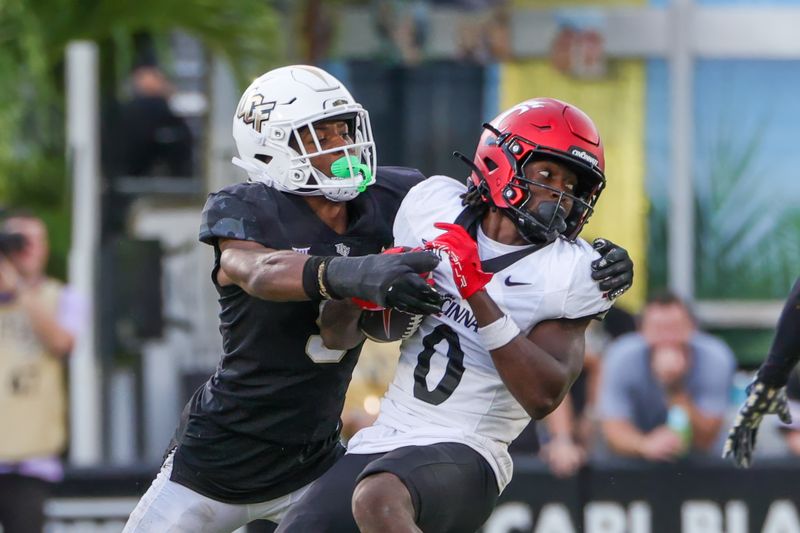 Oct 12, 2024; Orlando, Florida, USA; Cincinnati Bearcats wide receiver Tony Johnson (0) is tackled by UCF Knights defensive back Sheldon Arnold (9) during the second half at FBC Mortgage Stadium. Mandatory Credit: Mike Watters-Imagn Images