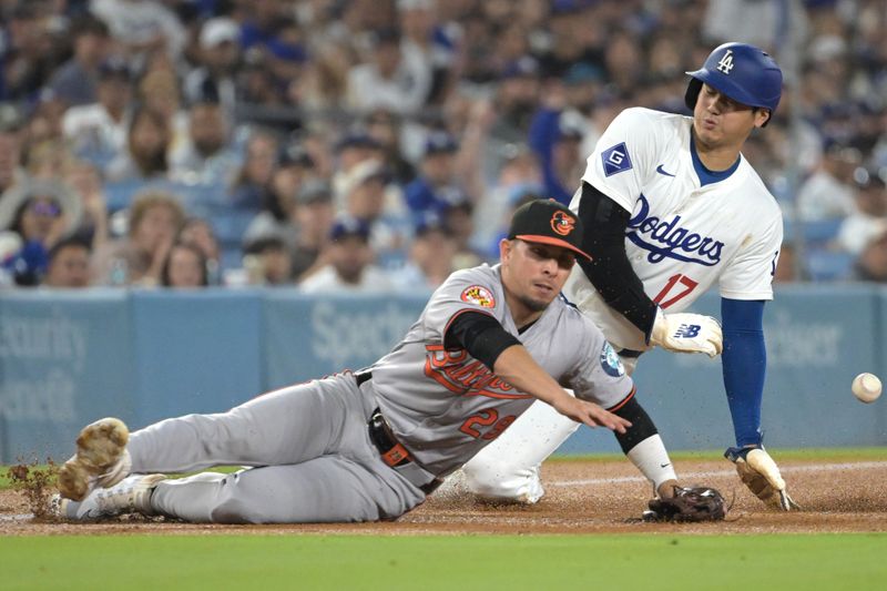 Aug 28, 2024; Los Angeles, California, USA;  The ball hits the dirt in front of Baltimore Orioles third baseman Ramon Urias (29) and gets Los Angeles Dodgers designated hitter Shohei Ohtani (17) in the left shoulder as he steals third in the third inning at Dodger Stadium. Mandatory Credit: Jayne Kamin-Oncea-USA TODAY Sports