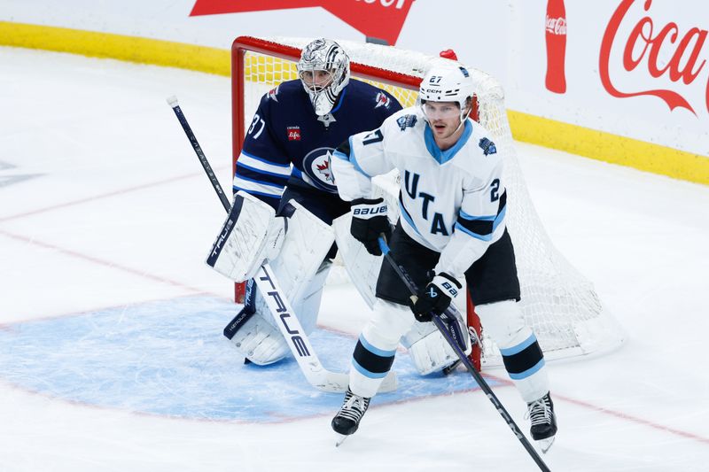 Nov 5, 2024; Winnipeg, Manitoba, CAN;  Winnipeg Jets goalie Connor Hellebuyck (37) and Utah Hockey Club forward Barrett Hayton (27) look for the puck during the third period at Canada Life Centre. Mandatory Credit: Terrence Lee-Imagn Images