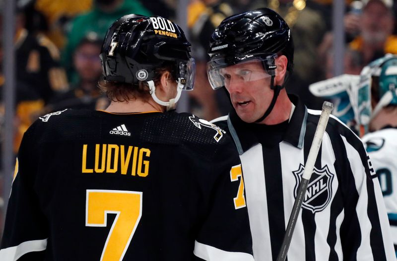 Mar 14, 2024; Pittsburgh, Pennsylvania, USA; Pittsburgh Penguins defenseman John Ludvig (7) talks with linesman David Brisebois (96) against the San Jose Sharks during the first period at PPG Paints Arena. Mandatory Credit: Charles LeClaire-USA TODAY Sports