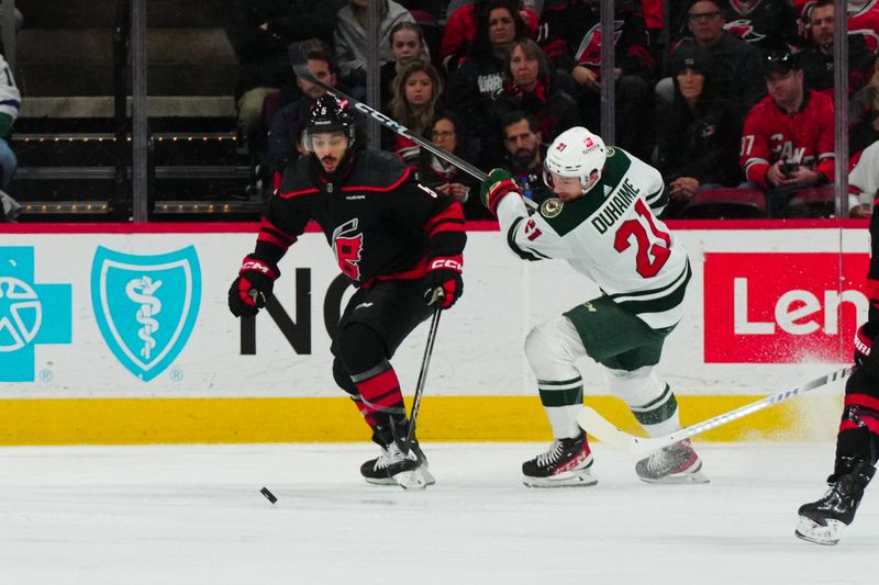 Jan 21, 2024; Raleigh, North Carolina, USA; Carolina Hurricanes defenseman Jalen Chatfield (5) and Minnesota Wild right wing Brandon Duhaime (21) battle over the puck during the first period at PNC Arena. Mandatory Credit: James Guillory-USA TODAY Sports