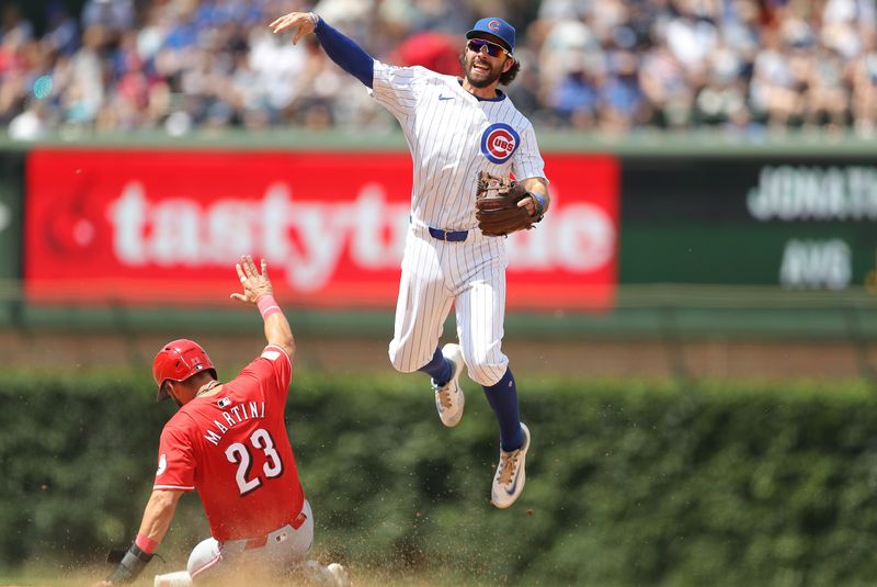 May 31, 2024; Chicago, Illinois, USA; Cincinnati Reds outfielder Nick Martini (23) slides as Chicago Cubs shortstop Dansby Swanson (7) throws the ball to first base for a double play during the fourth inning at Wrigley Field. Mandatory Credit: Melissa Tamez-USA TODAY Sports