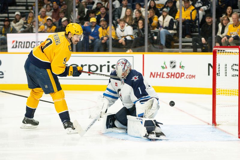 Nov 23, 2024; Nashville, Tennessee, USA;  Winnipeg Jets goaltender Eric Comrie (1) blocks the shoot if Nashville Predators left wing Filip Forsberg (9) during the third period at Bridgestone Arena. Mandatory Credit: Steve Roberts-Imagn Images