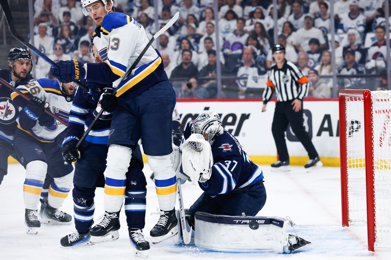 Apr 30, 2025; Winnipeg, Manitoba, CAN; Winnipeg Jets goalie Connor Hellebuyck (37) makes a save despite a screen by St. Louis Blues forward Alexey Toropchenko (13) during the first period in game five of the first round of the 2025 Stanley Cup Playoffs at Canada Life Centre. Mandatory Credit: Terrence Lee-Imagn Images