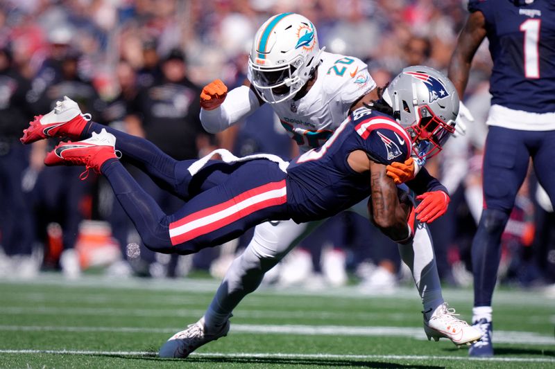 New England Patriots wide receiver DeMario Douglas hangs onto the ball as Miami Dolphins linebacker Jordyn Brooks (20) tries to block during the first half of an NFL football game, Sunday, Oct. 6, 2024, in Foxborough, Mass. (AP Photo/Steven Senne)