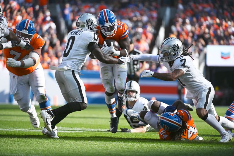 Denver Broncos running back Javonte Williams (33) is tackled by Las Vegas Raiders cornerback Jakorian Bennett (0) and safety Tre'von Moehrig (7) during the second half of an NFL football game, Sunday, Oct. 6, 2024, in Denver. (AP Photo/Geneva Heffernan)