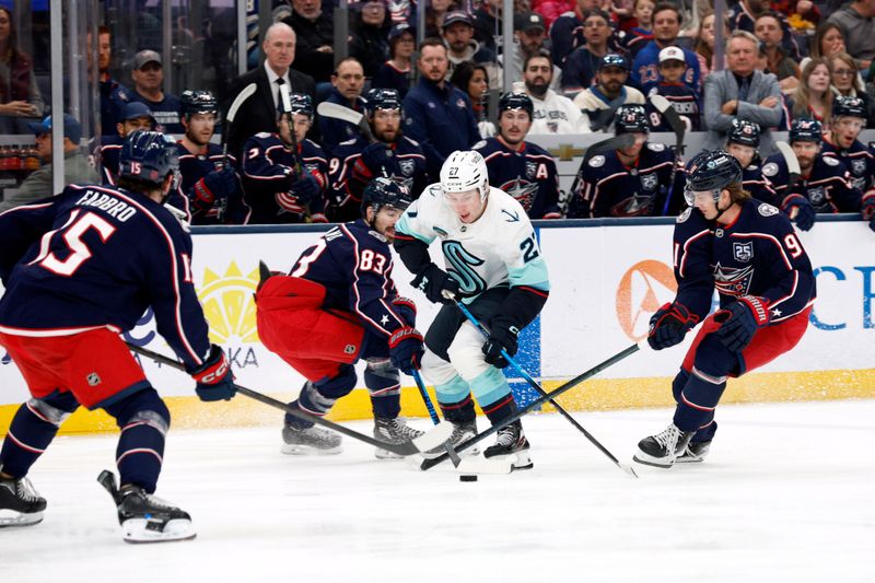 Mar 21, 2026; Columbus, Ohio, USA; Seattle Kraken center Berkly Catton (27) carries the puckpast Columbus Blue Jackets center Kent Johnson (91) and Columbus Blue and right wing Conor Garland (83) during the first period at Nationwide Arena. Mandatory Credit: Russell LaBounty-Imagn Images