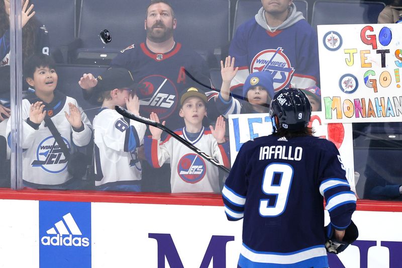 Mar 11, 2024; Winnipeg, Manitoba, CAN; Winnipeg Jets left wing Alex Iafallo (9) tosses a puck to a fan before a game against the Washington Capitals at Canada Life Centre. Mandatory Credit: James Carey Lauder-USA TODAY Sports