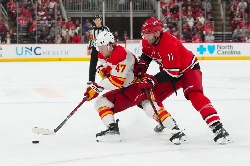 Nov 30, 2025; Raleigh, North Carolina, USA;  Calgary Flames center Connor Zary (47) tries to control the puck gains the che3ck by Carolina Hurricanes center Jordan Staal (11) during the second period at Lenovo Center. Mandatory Credit: James Guillory-Imagn Images