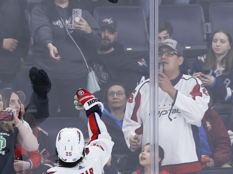 Mar 11, 2024; Winnipeg, Manitoba, CAN; Washington Capitals defenseman Ethan Bear (25) tosses a puck to a fan before a game against the Winnipeg Jets at Canada Life Centre. Mandatory Credit: James Carey Lauder-USA TODAY Sports