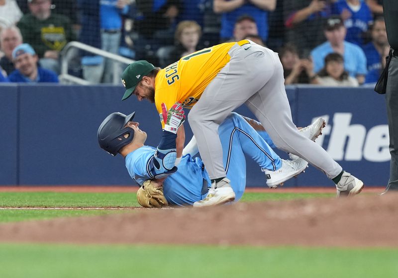 May 31, 2025; Toronto, Ontario, CAN; Athletics third baseman Max Schuemann (12) tags out and helps Toronto Blue Jays centre fielder Daulton Varsho (5) after grabbing his left leg after rounding second base against the Athletics during the third inning at Rogers Centre. Mandatory Credit: Nick Turchiaro-Imagn Images