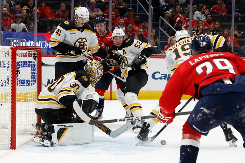 Oct 5, 2024; Washington, District of Columbia, USA; Boston Bruins goaltender Brandon Bussi (30) makes a save in front of Bruins center John Beecher (19) and Washington Capitals center Hendrix Lapierre (29) in the third period at Capital One Arena. Mandatory Credit: Geoff Burke-Imagn Images