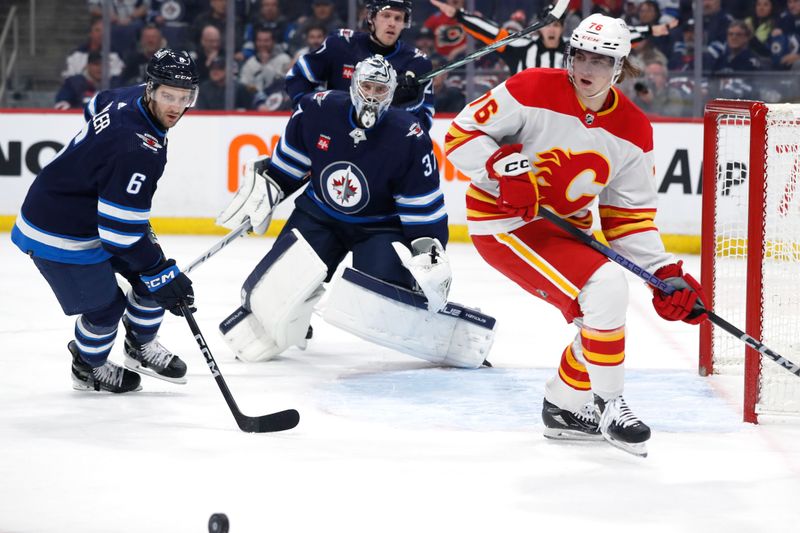 Apr 4, 2024; Winnipeg, Manitoba, CAN; Winnipeg Jets defenseman Colin Miller (6), Winnipeg Jets goaltender Connor Hellebuyck (37) and Calgary Flames center Martin Pospisil (76) eye a bouncing puck in the first period at Canada Life Centre. Mandatory Credit: James Carey Lauder-USA TODAY Sports