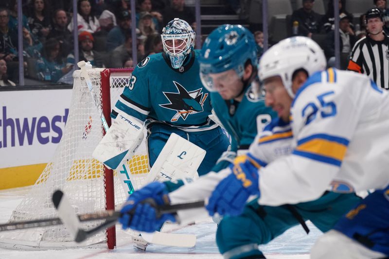 Mar 6, 2026; San Jose, California, USA; San Jose Sharks goaltender Alex Nedeljkovic (33) defends the goal as defenseman Sam Dickinson (6) and St. Louis Blues right winger Jordan Kyrou (25) pursue the puck in the first period at SAP Center at San Jose. Mandatory Credit: David Gonzales-Imagn Images